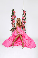 Beautiful natural woman in elegant long dress on a floral swing on white background. Glamour female...