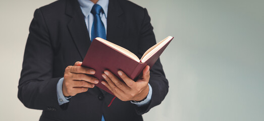 Businessman in a suit reading a book while standing against a gray background