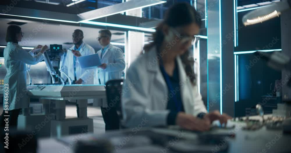 Poster Rack Focus Switching from a Female Engineer Working on Electronic Circuit Boards to Industrial Robotics Specialists in Lab Coats Working on a Mobile AI Robot in a Tech Factory Facility