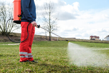 Farmer spraying pesticide on lawn field wearing protective clothing. Treatment of grass from weeds...