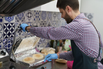 The cook toasting pita bread on a press grill in the commercial kitchen. Male person cooking gyros snacks in a Greek fast food restaurant
