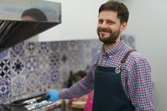 Portrait of friendly white man in apron cooking food in a commercial kitchen. Cheerful Caucasian male person preparing food in a electric grill press