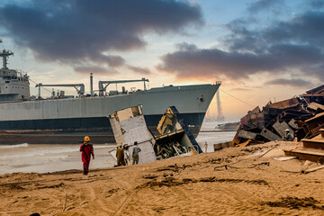 Shipbreaking yard and iron scrap in the harbor, with the background of a shipwreck and sunset at...