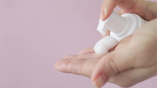 Facial foam dispenser in female hands, face cleanser, beauty cosmetic for skin care, woman squeezes facewash mousse