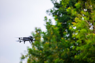 Modern drone flies in the forest. Dark drone in the air against