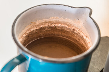 Ein blauer Becher aus Emaile mit Wasser und sehr starken Kalkablagerungen auf der Innenseite, Deutschland