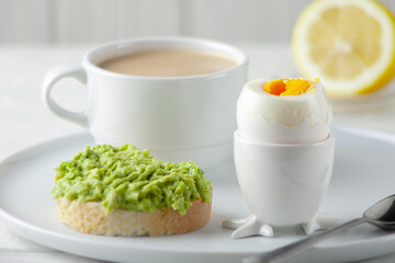Soft-boiled egg with avocado sandwich and a cup of coffee with cream and on the table. European breakfast.