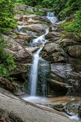 a tall waterfall running through a forest filled with green trees