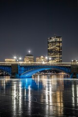 Naklejka premium night time on the riverbank and the blue bridge with lights reflecting in it