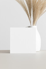 Square invitation card mockup with a pampas decoration on the beige table.