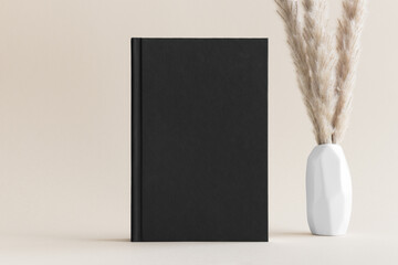 Black book mockup with a pampas decoration on the soft yellow background.