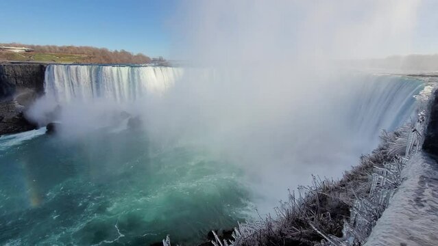 Water flowing down in mesmerizing Niagara Falls to the river surrounded with frosty plants, Canada