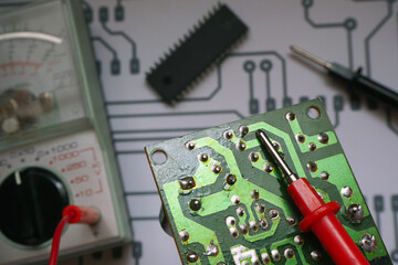 Electronic repair bench. Electronic circuit board with blurred multimeter, chip and diagram background. Focused on red probe.