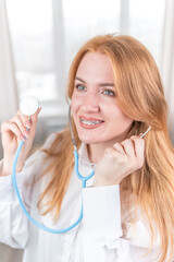 Medical concept. Smiling nurse with braces and a stethoscope in her hand. Happy and laughing female doctor in a white coat posing at the camera. Hospital worker