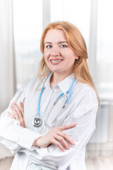 Medical concept. Smiling nurse with braces and a stethoscope in her hand. Happy and laughing female doctor in a white coat posing at the camera. Hospital worker