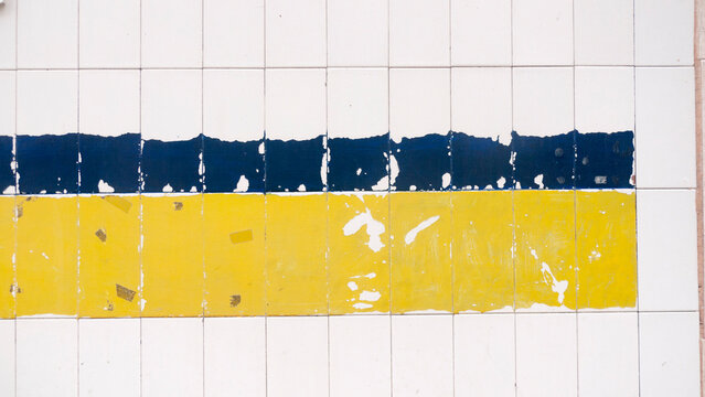 Restos de pegatina azul y amarilla en pared de azulejo blanco