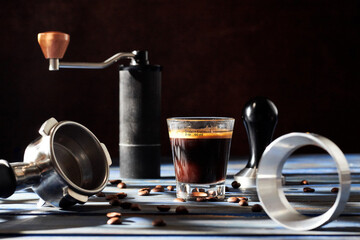Fresh glass cup of espresso coffee, manual coffee grinder, portafilter and coffee utensil on blue...