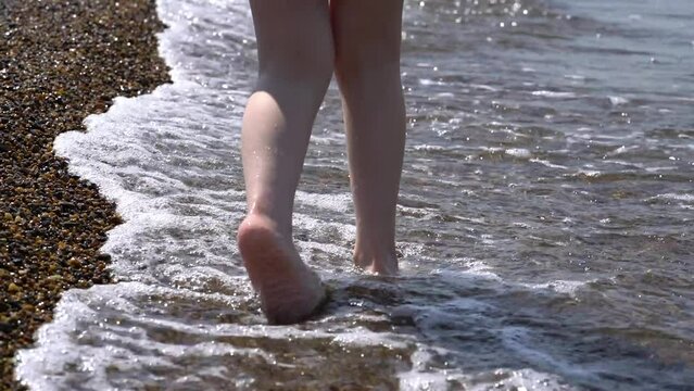 The child is walking along the lake. Waves wash children's feet.