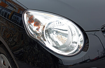 Close-up front headlight with xenon light of black modern car.