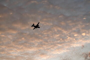 Silhouette of a military airplane flying in the clouds at sunset in Coronado, San Diego.
