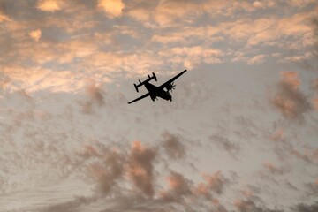 Fototapeta na wymiar Low angle shot of a silhouette of the Coronado San Diego military airplane flying in a sunset sky