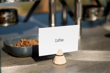 Closeup shot of a paper coffee sign near a bowl of coffee beans
