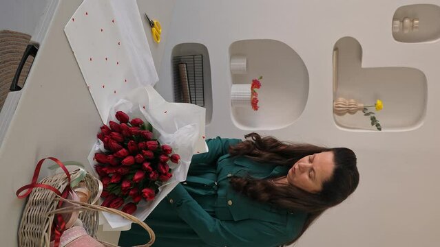 Caucasian lady florist collects a lush bouquet of tulips. A professional makes a fresh bouquet. Small business. Vertical video.