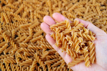 Heap of Dried Whole Wheat Fusilli Pasta in Hand with Blurry Pasta in Background
