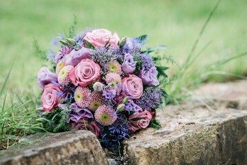 Bouquet of pink and purple flowers decorated with greenery on stone ground with grass.