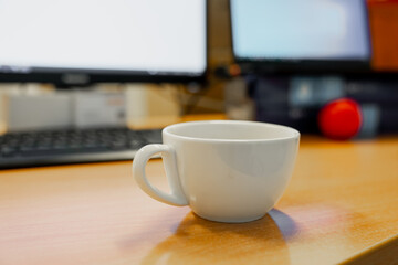 White coffee mug in the morning next to two monitors in background