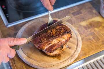 Real hearty homemade roast pork is cut into portions on a wooden board in the kitchen, Germany