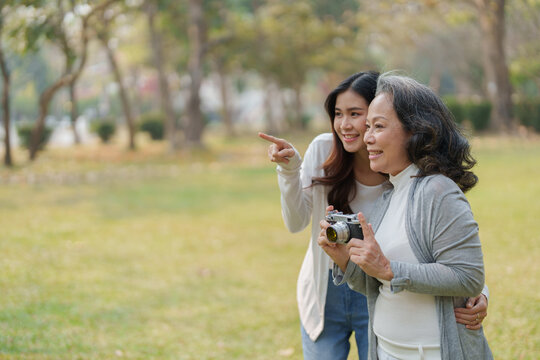 Asian teenage mother and daughter walking in park with camera to capture memories