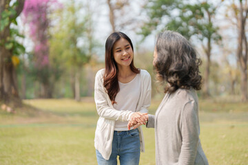 Adult daughter holding her elderly mother hand with love and walk together in park