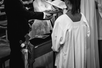 Grayscale shot of the bride and the groom in front of priest during the marriage mass at the church