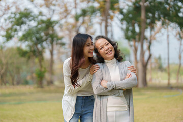 Fototapeta premium Grown daughter with aging mother showing love and walking together in the parkland