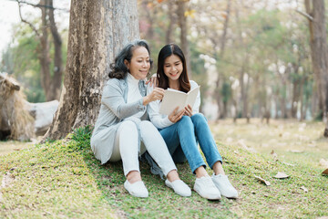Fototapeta premium Grown daughter with aging mother expressing love and looking at memory notebook under tree in public park