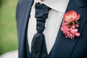 Closeup of the groom's black tie with a pink boutonniere on a black suit