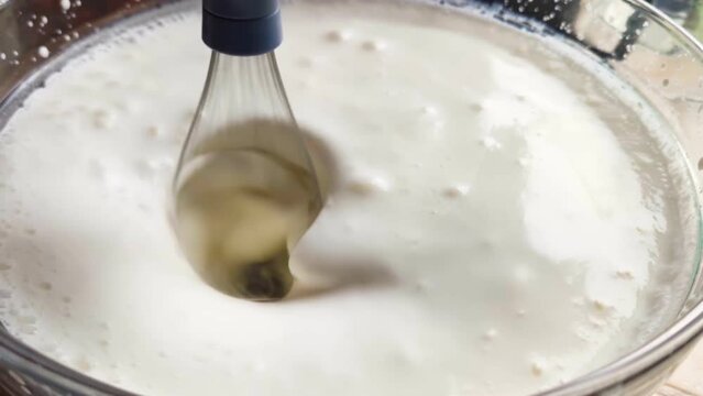 A wire whisk whisks milk in a bowl. Mixing whipped cream and eggs. White bubbling liquid due to blender operation. Close-up and slow-mo effect