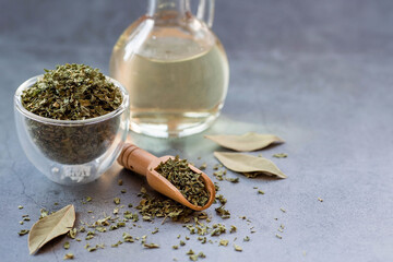 Fragrant spices. Dried parsley, bay leaf and a bottle of oil on a gray background. Free space.