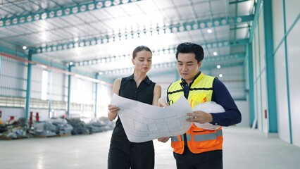 Professional Asian male architect holding paper blueprints of factory design talking with woman...