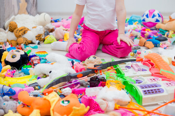 many toys are scattered on the floor in a big pile. The girl plays with toys. Different children, hands, large and small animals, a house.