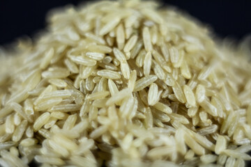 Studio macro shot of a pile of brown rice, also called complete, integral or wholegrain rice, with a blurred background. Brown rice is richer in fiber and used in several diets.