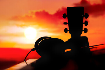 silhouette of synthesizer , acoustic guitar neck and headphones  at colorful sunset