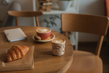 Cappuccino in beautiful ceramic mugs, croissant on the table in a cozy cafe. 