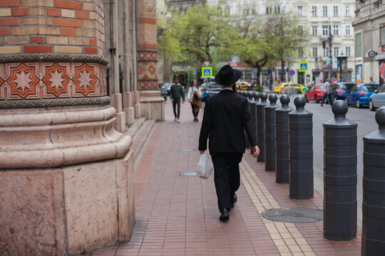 Orthodox Jewish person wearing traditional black costume from behind walking along synagog in the street