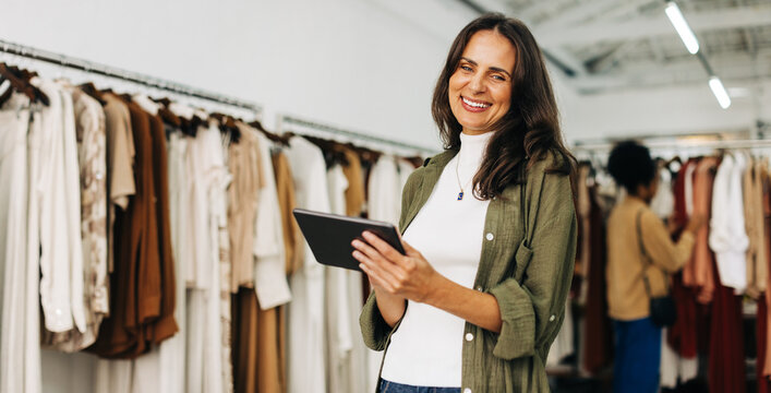 Happy clothing store owner using a tablet to manage her small business