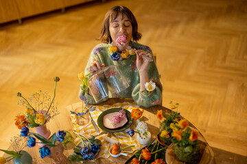 Young woman has a dinner with flowers, sitting by the table full of different flowers in vases and plate as a meal. Concept of beauty and flower diet