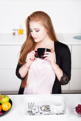 Young beautiful woman enjoying fresh aromatic coffee while sitting at a table in a modern kitchen.