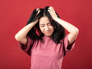A portrait of a young Indonesian (Asian) woman wearing a pink shirt, looking dizzy and holding her head with both hands. Isolated with a red background
