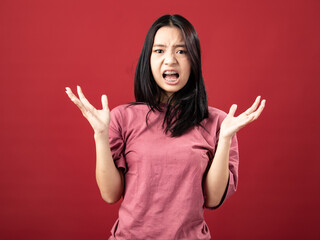 A portrait of a young Indonesian (Asian) woman wearing a pink shirt, seen frustrated and angry. Isolated with a red background